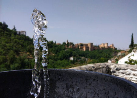Water flowing from the fountain cached in a moment. With Granada and beautiful blue sky in the background.の写真素材