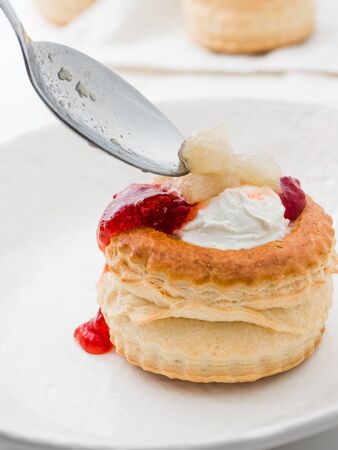 Canape vol-au-vents being filled with cream and jam on a white plateの写真素材