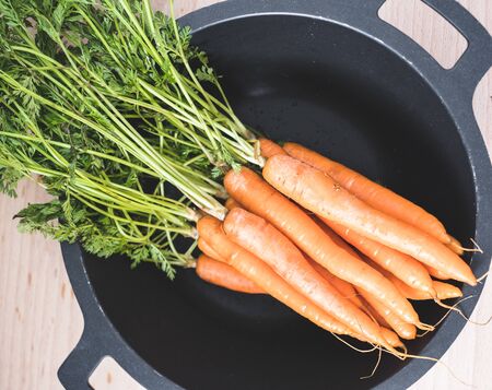 Bunch of organic carrots with leafs in a black wokの写真素材