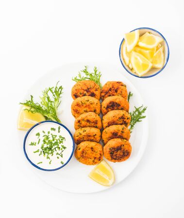 Fish cakes on a plate with lemon wedges, salad and sauce. Top view white background.の写真素材