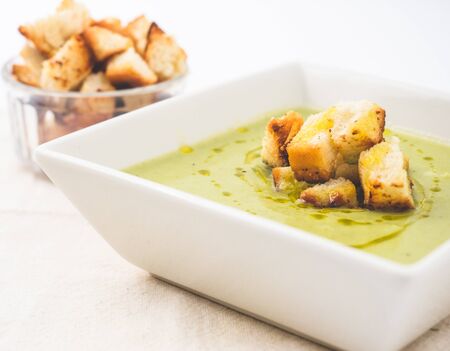 Green vegetables soup and croutons served in a white plate with olive oil. Side angle with white background.の写真素材