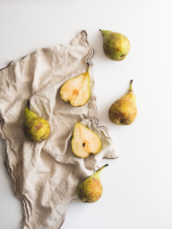 Whole pears and cut pears together with a cloth and a knife over a white counterの写真素材