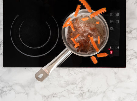 Spiral pasta falling into a pot with boiling water. Pot on top of the stove view from above.の写真素材