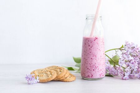 Berry smoothie in a glass jar with a straw for cocktails, cereal cookies, a branch of lilac, on a light background. Healthy lifestyle, diet, detox. Refusal of plastic. Daylight, selective focus.の写真素材