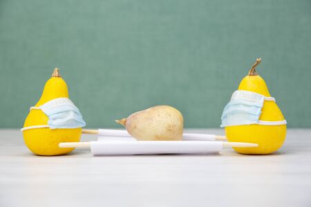 Zucchini under a medical face mask on a green background. Yellow pear. Decorative vegetables. Patient on a stretcher. Vegetables. Coronavirus, pandemic, quarantine. Harvest 2020. Covid-19. Allergyの写真素材