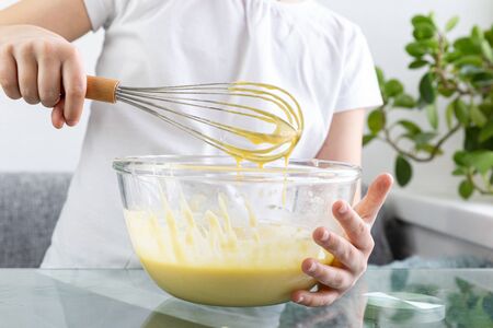 A close-up of the upper body of a child stirs the wafer dough by hand. Stir a delicious dough of flour, eggs, milk and sugar with a whisk. The dough is ready to cook. Children's cook.の写真素材