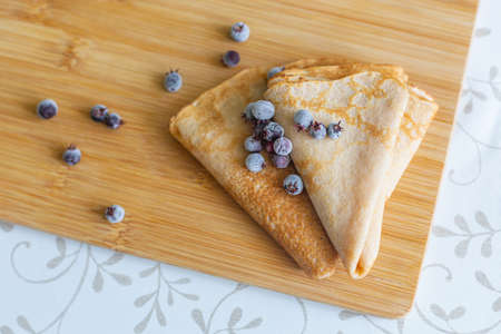 Two pancakes and frozen shadberry berries on a cutting board, top view. Traditional cuisine,...