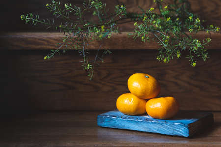Three juicy orange tangerines, a blue cutting board, branch of greens lie on a brown wooden staircase. Still life of fruits. New year, christmas.の写真素材