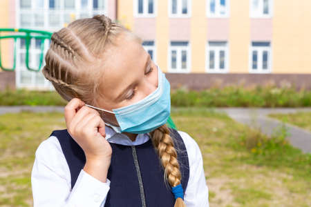 Portrait of a girl in a school uniform in a blue medical mask on background of a building.の写真素材