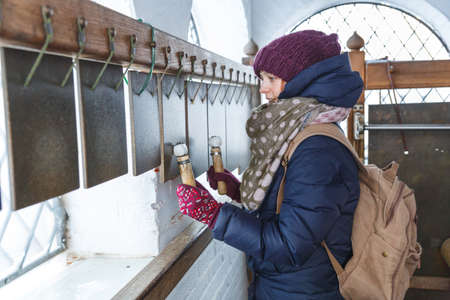 Girl in winter clothes on bell tower or belfry rings bells, hits iron plates with sticks. Church,...
