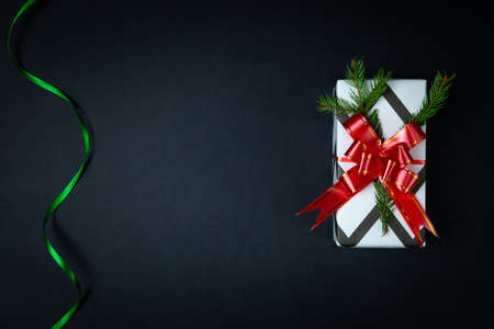 Christmas gift, red bow, fir branch on a black background. Satin spiral green ribbon. Christmas...