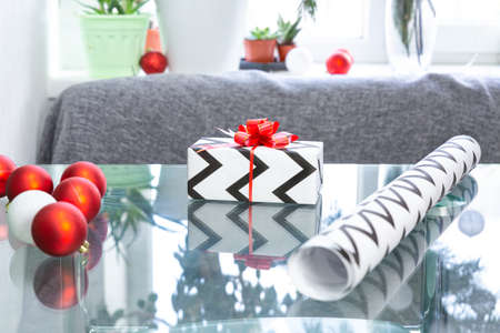 Christmas gift, wrapping paper, Christmas balls on a glass table against the background of a window...