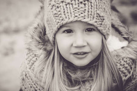 Portrait of a beautiful little girl 4-5 years old close-up in warm clothes and a knitted hat. Child in fashionable winter clothes. Knitting for children. Monochrome, sepia, copy space.の写真素材