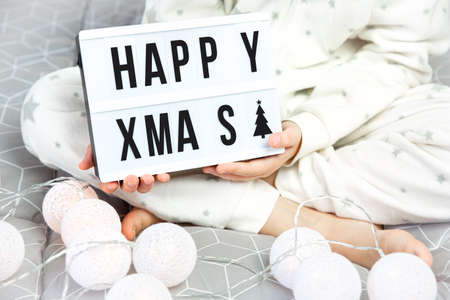 A child in white pajamas with asterisks sits cross-legged on the bed and holds a light board with...