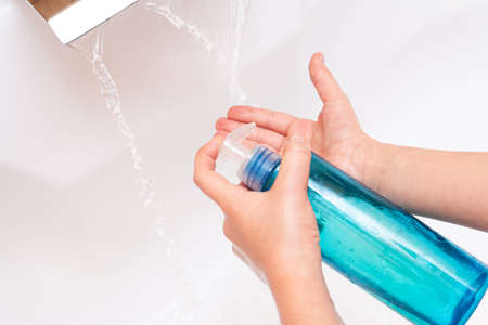 A child pours soap or antiseptic on his hands under a tap with clean water close-up on a white...