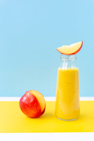 Yellow smoothie in a glass jar, a slice of nectarine on a yellow, sky blue background. Healthy nutrition, detox, vegan.の写真素材
