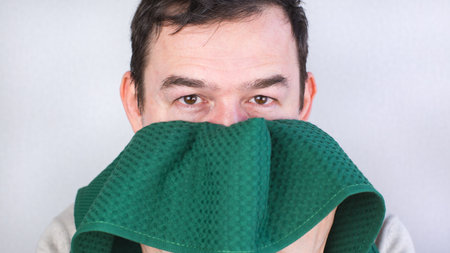 Close-up of a Caucasian man wiping his face with a green towel.