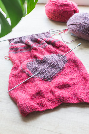 On a light background are clews of wool thread and hand knitting with a heart.