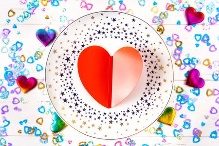A plate with stars and a red heart on a background of sequins and rainbow heartsの写真素材