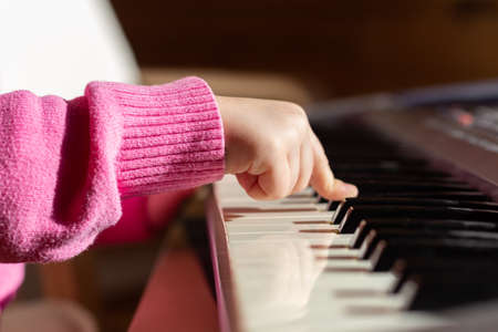 Close-up childs hand on piano or synthesizer keys, side view.の写真素材