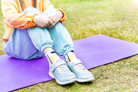 Child sitting on a sports mat outdoors, hugging her knees with her arms.の写真素材