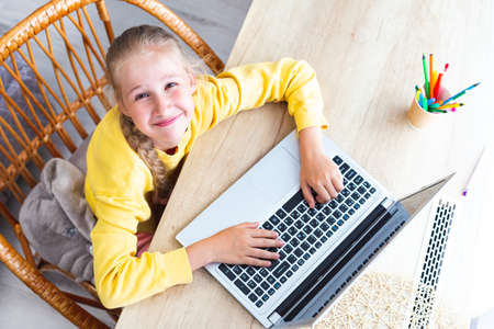 Caucasian girl sits at a desk, hands on laptop keyboard, smiles, top view.