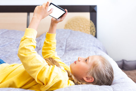Teenage girl lying on the bed with a smartphone in her hands. White screen.の写真素材