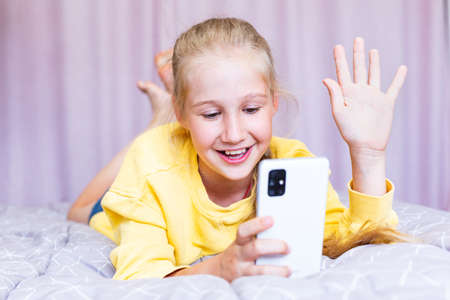 A blonde Caucasian teenage girl with a phone in her hands, lying on the bed, blogging, Communicating...