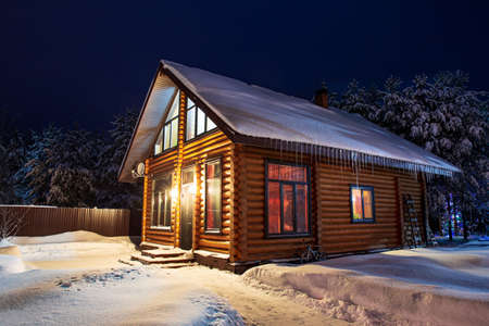 Rustic log house, snow-covered pine trees, snowdrifts, fabulous winter night. Rural beautiful winter landscape. Rent suburban housing, real estate. New Year, Christmas.の写真素材