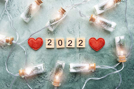 Number 2022 on wooden squares and a glowing garland of glass jars with Christmas trees and snow...