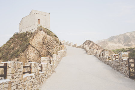A road with a stone fence going up to the old tower on the top of the mountain, sepia. Historical places. Way up. Travel, hiking. Mountains Akhulgo, Memorial Historical Complex, Dagestan.の写真素材