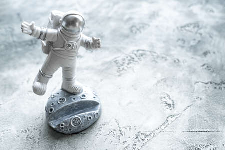 Miniature astronaut balancing on moon in spacesuit waving his hand. Phone stand in form of cosmonaut. World Day of Aviation and Cosmonautics. Science fiction, science and space exploration, future.の写真素材