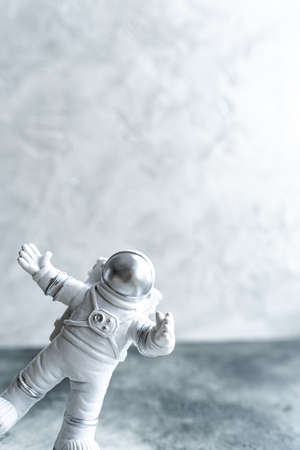 Trendy Miniature astronaut in spacesuit, peeking around corner waving his hand on gray textured background, vertical, copy space. World Day Cosmonautics. Science and space exploration, future.の写真素材
