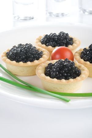 Tartlet with black caviar on a white platter, decorated with cherry tomatoes and green onionsの写真素材