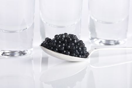 Silver spoon of black caviar and three glass of vodka over white backgroundの写真素材