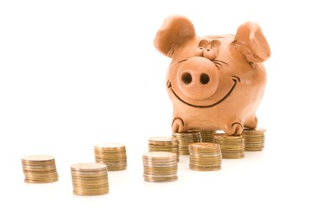 Pig bank seat on a stack of coins isolated over white backgroundの写真素材