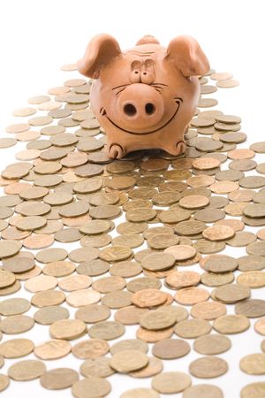 Pig bank seat on a heap of coins isolated over white backgroundの写真素材