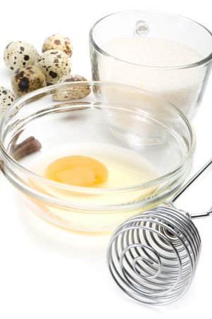 Dish of liquid egg, sugar, whisk and quail eggs over white backgroundの写真素材