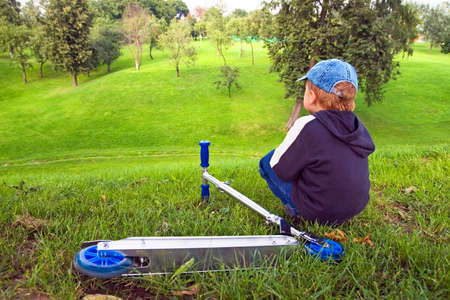 The boy looks afar. Beside lays scooterの写真素材