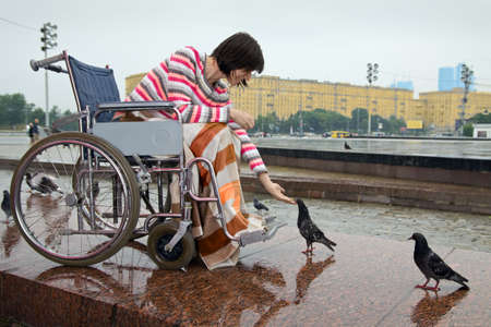Woman in wheelchair feeds pigeons in street citiesの写真素材