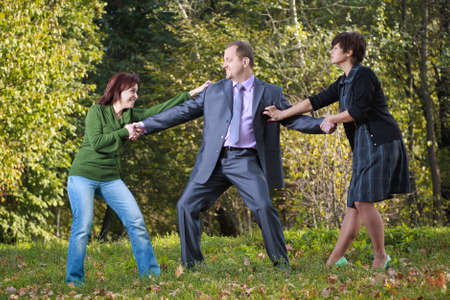 Two women pulling a man in opposite sidesの写真素材