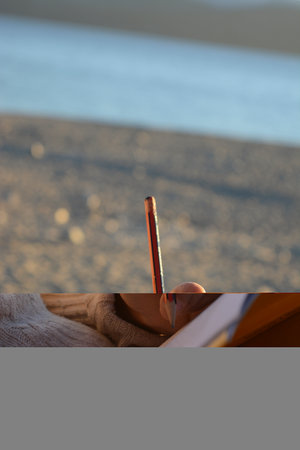 Close-up of a woman's hand holding a pencil while drawing a picture on the beach