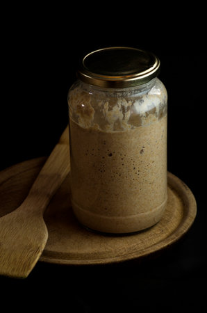 sourdough sourdough for bread baking, with wooden spoon and rolling pin on black background