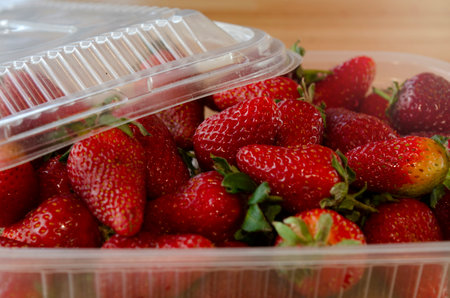 very red and ripe strawberries in plastic tray on wooden tableの写真素材