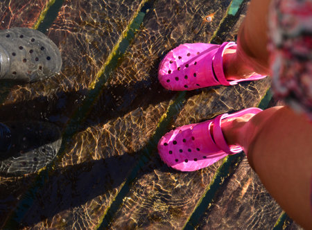 feet with pink and black rubber shoes in the crystal clear water of a lake, on wooden pierの写真素材