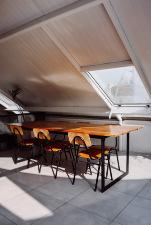 Interior of modern house, dining room with wooden table and chairs in the attic with one window...