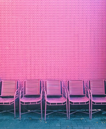 Pink chairs lined up in front of pink wall made from recycled cassette tapesの写真素材