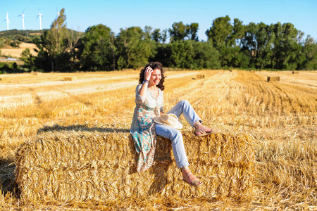 Beautiful woman sitting on a haystack in a wheat field.の写真素材