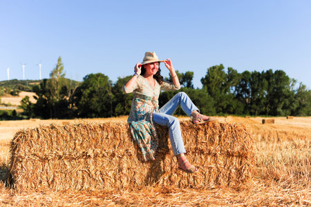 Beautiful woman sitting on a haystack in a wheat field.の写真素材