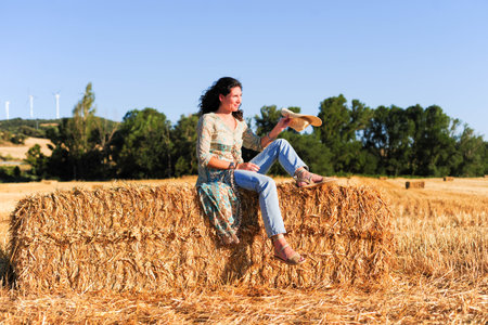 Beautiful woman sitting on a haystack in a wheat field.の写真素材